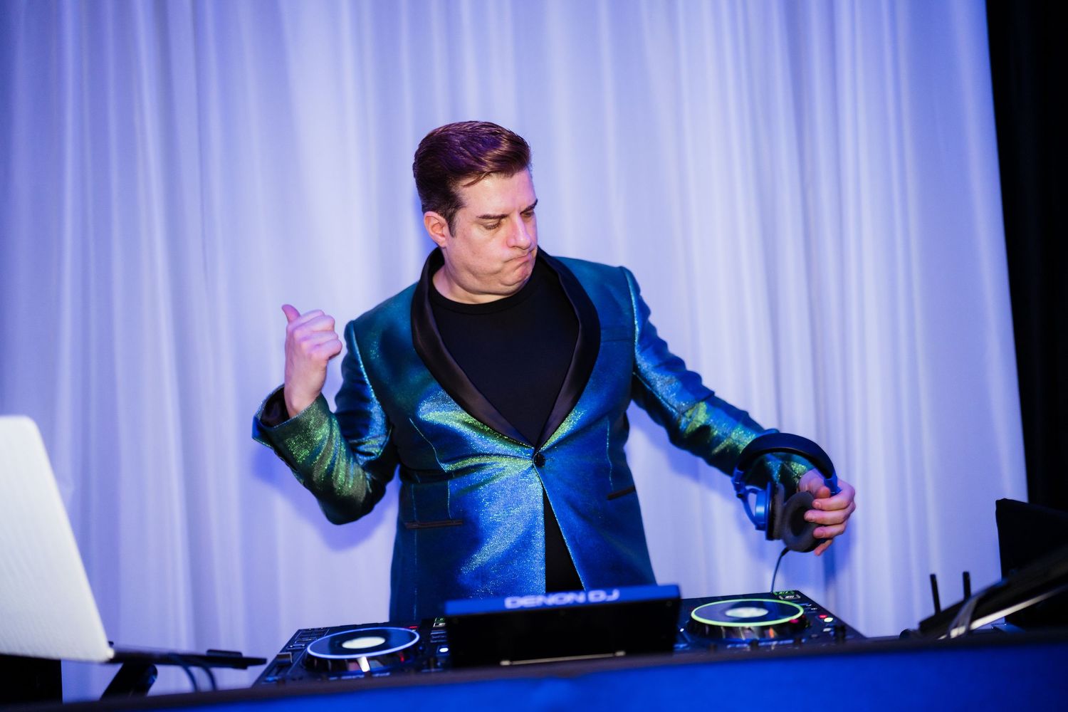 A DJ performs at a venue with blue lighting and white drapes behind the booth.