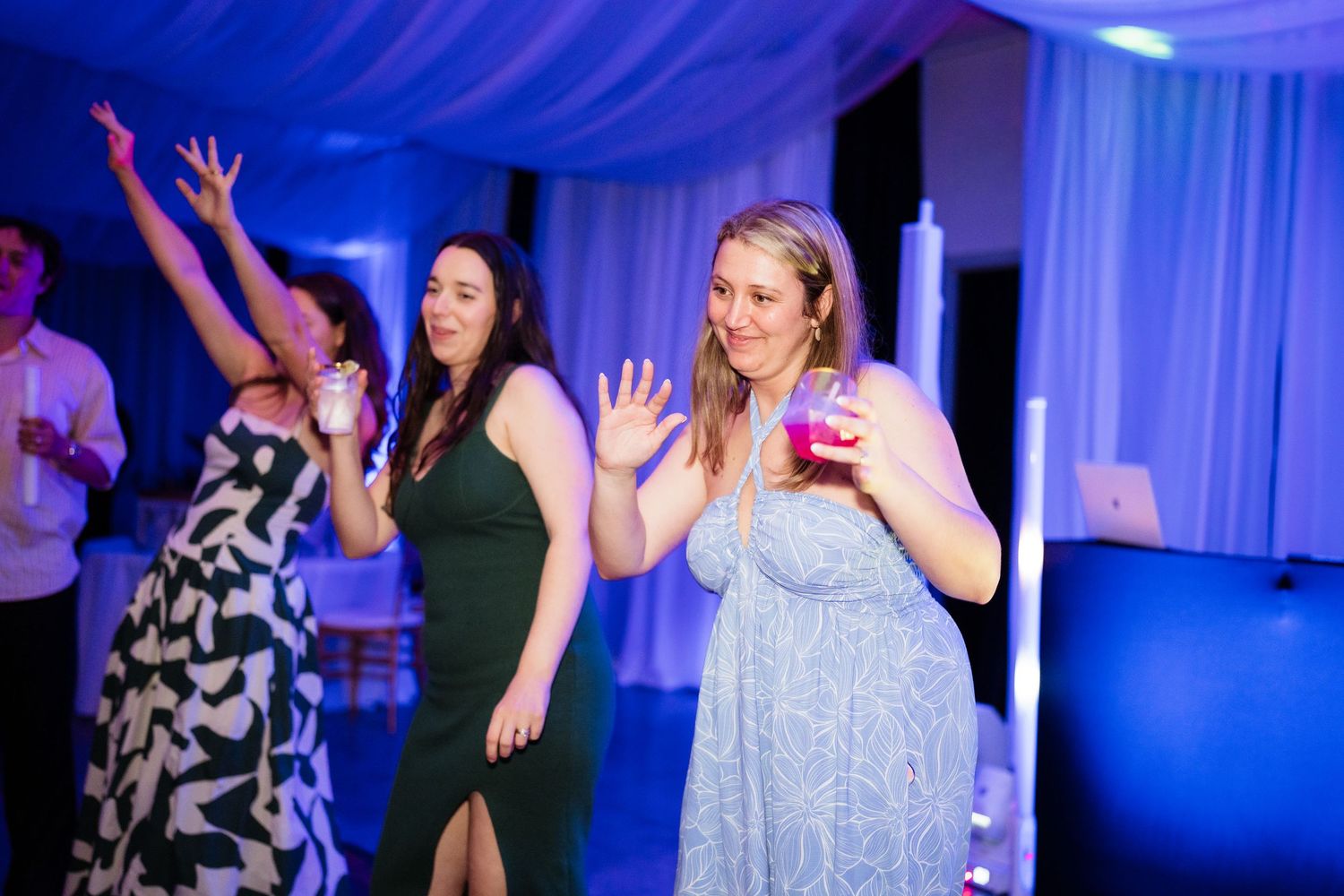 Wedding reception guests dancing and celebrating under dramatic blue lighting and white draped ceiling.