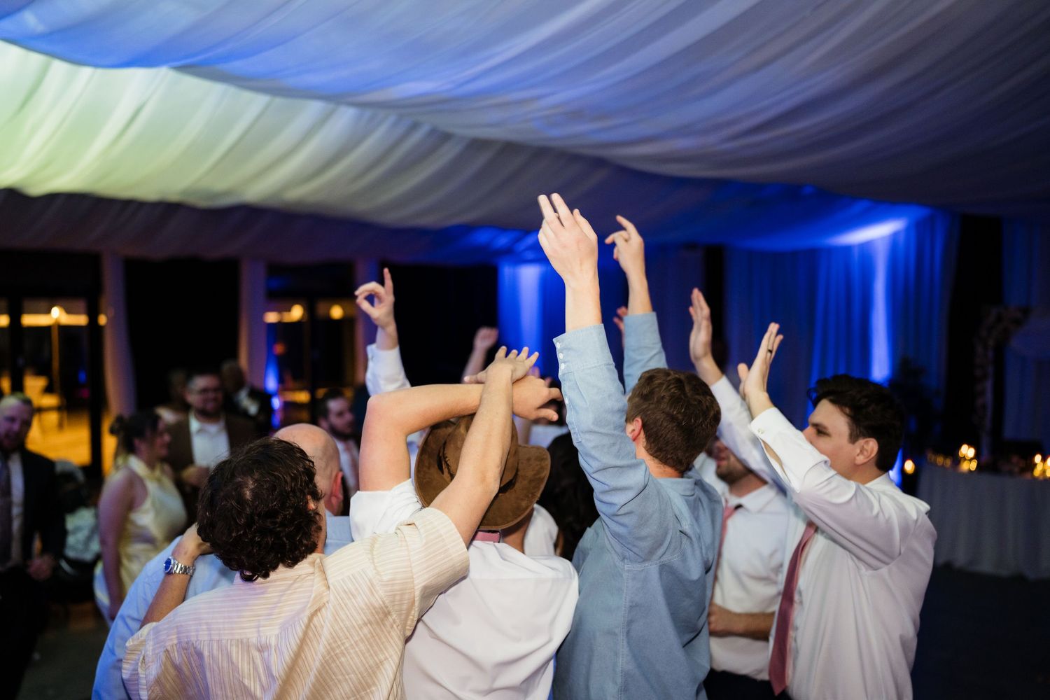 Wedding reception dance floor filled with guests dancing with hands raised under dramatic blue lighting.