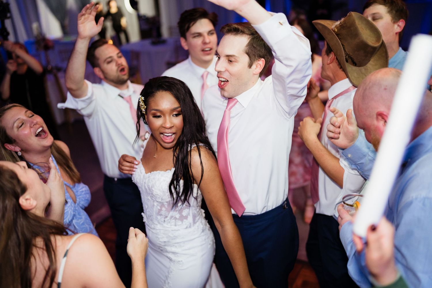 Wedding guests dance and celebrate joyfully during a reception party with a purple-lit dance floor.