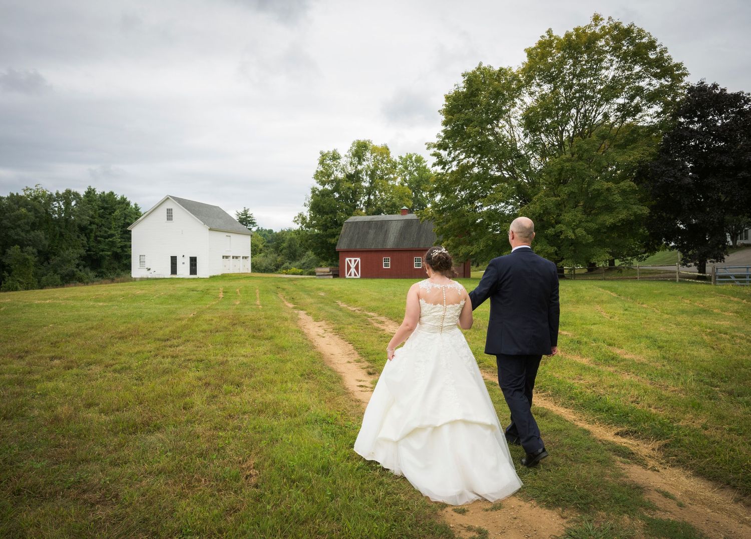 A wedding couple poses in front of a white farmhouse venue with snow-covered grounds on a winter day.