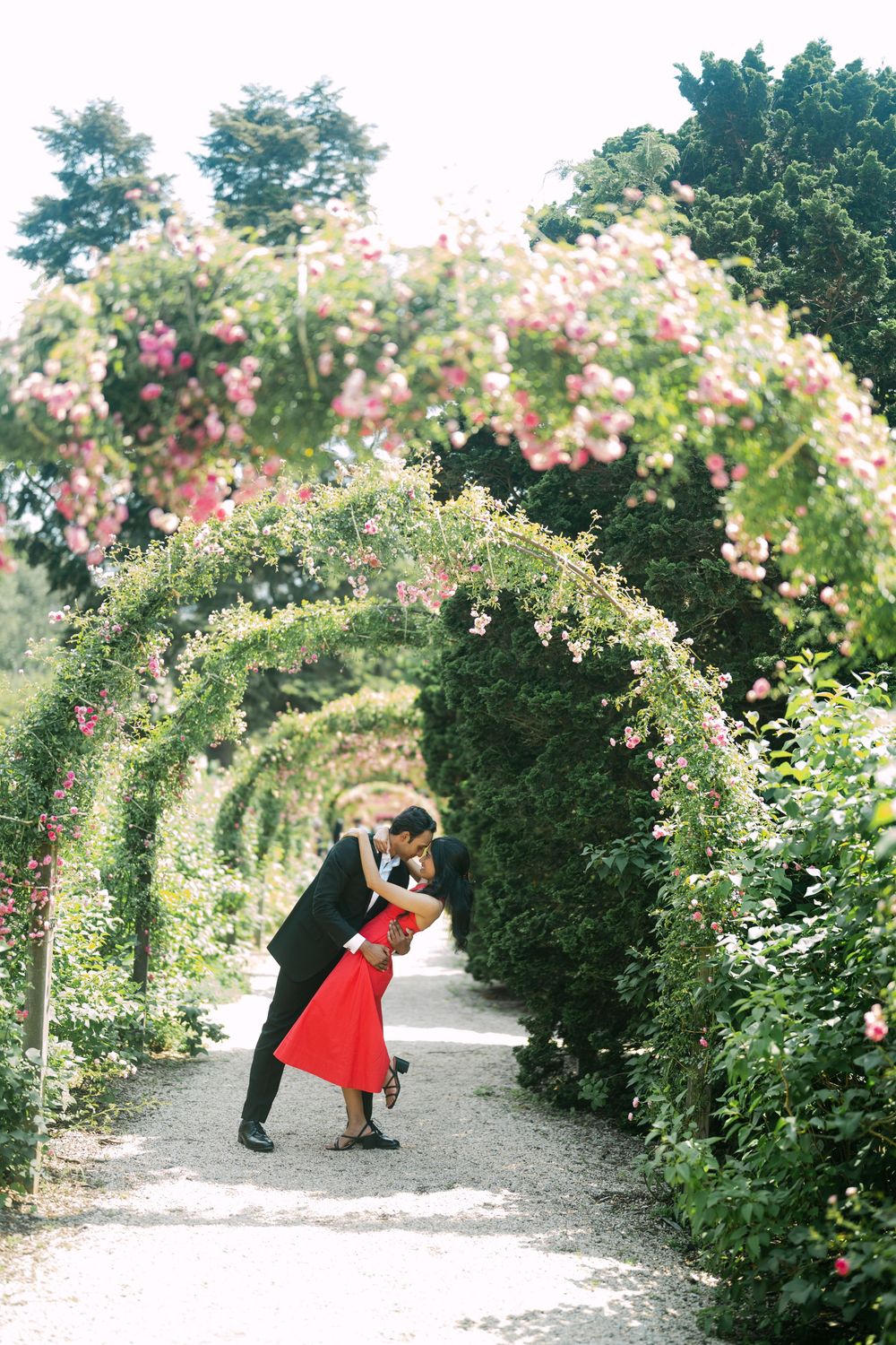 A romantic moment captured in a rose garden walkway with flowering arches overhead.