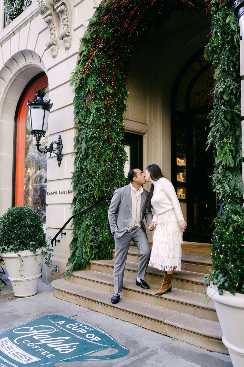 Wedding guests gather on elegant stone steps decorated with greenery and lanterns outside a luxury venue entrance.