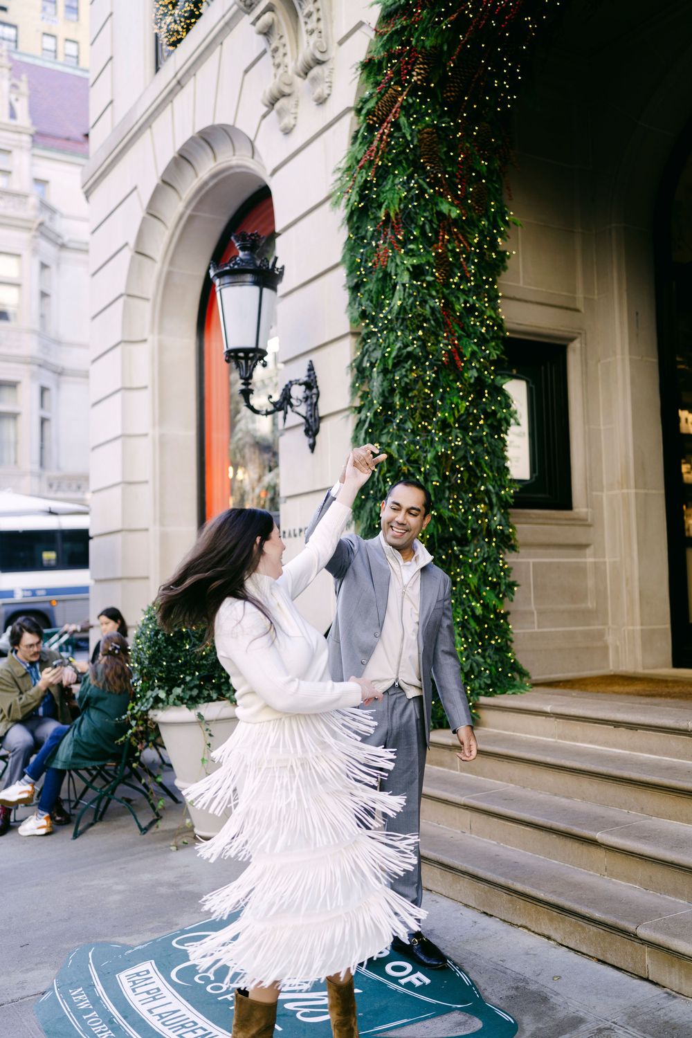 A person in a flowing white dress twirls on the steps of a historic building with ivy-covered walls.
