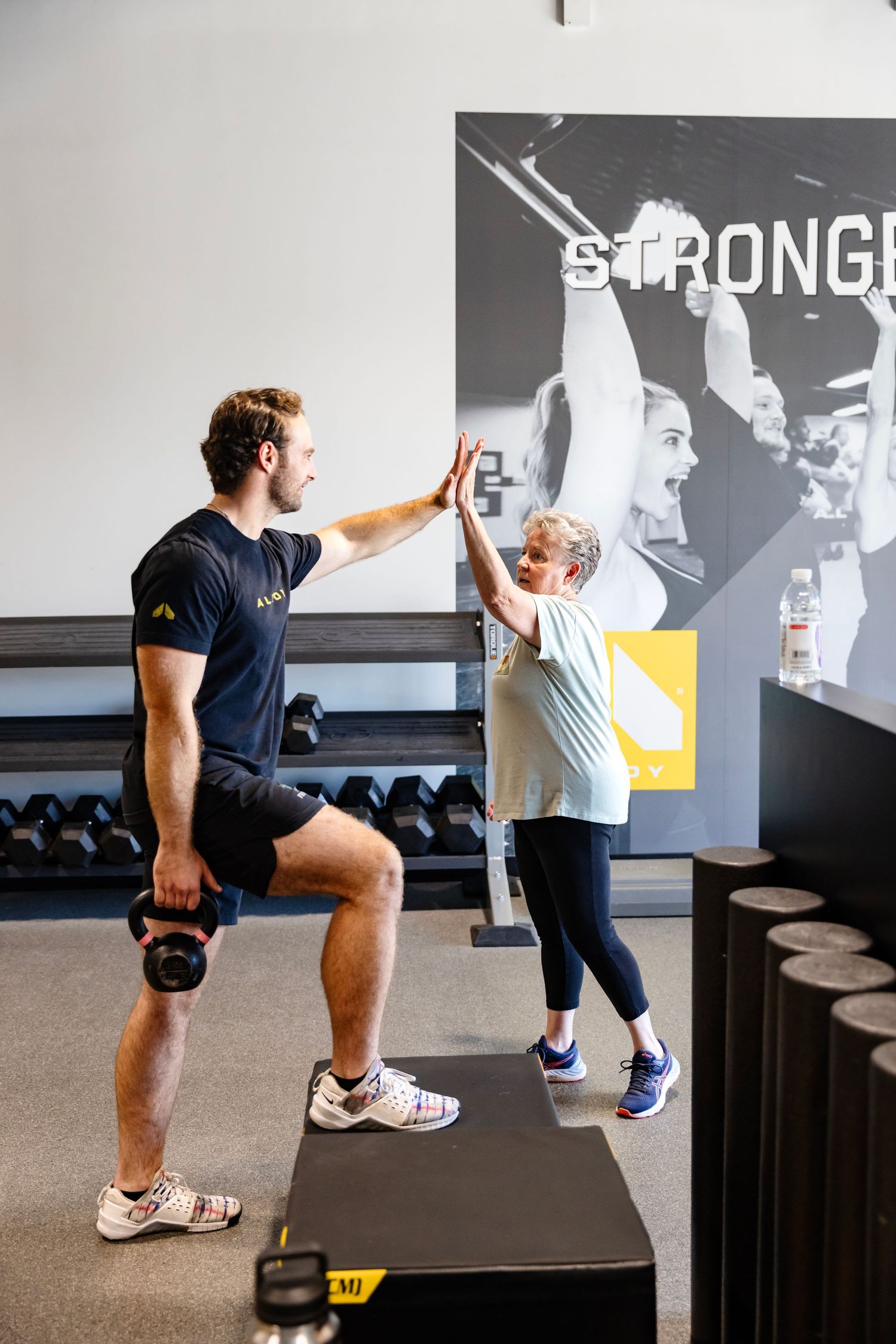Two people demonstrate a series of partner-assisted stretching exercises in a gym setting with kettlebells and equipment.