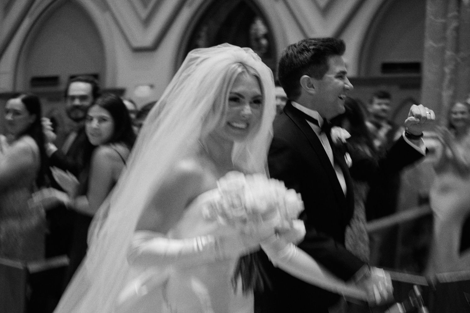 A joyful bride in a white wedding dress and veil smiles while holding a bouquet during a traditional church ceremony.