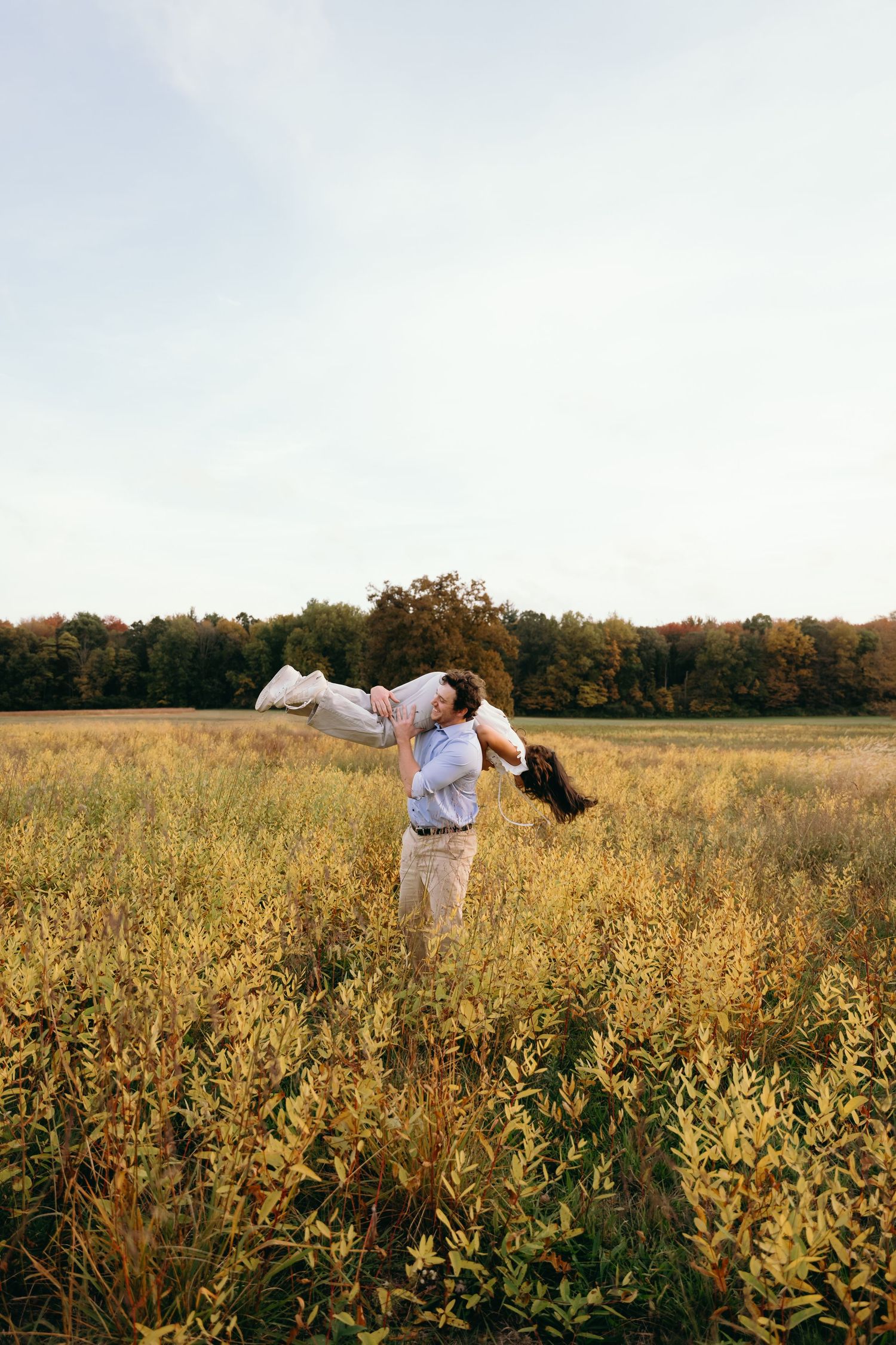 A couple in white outfits dances gracefully in a golden field of tall grass during sunset.