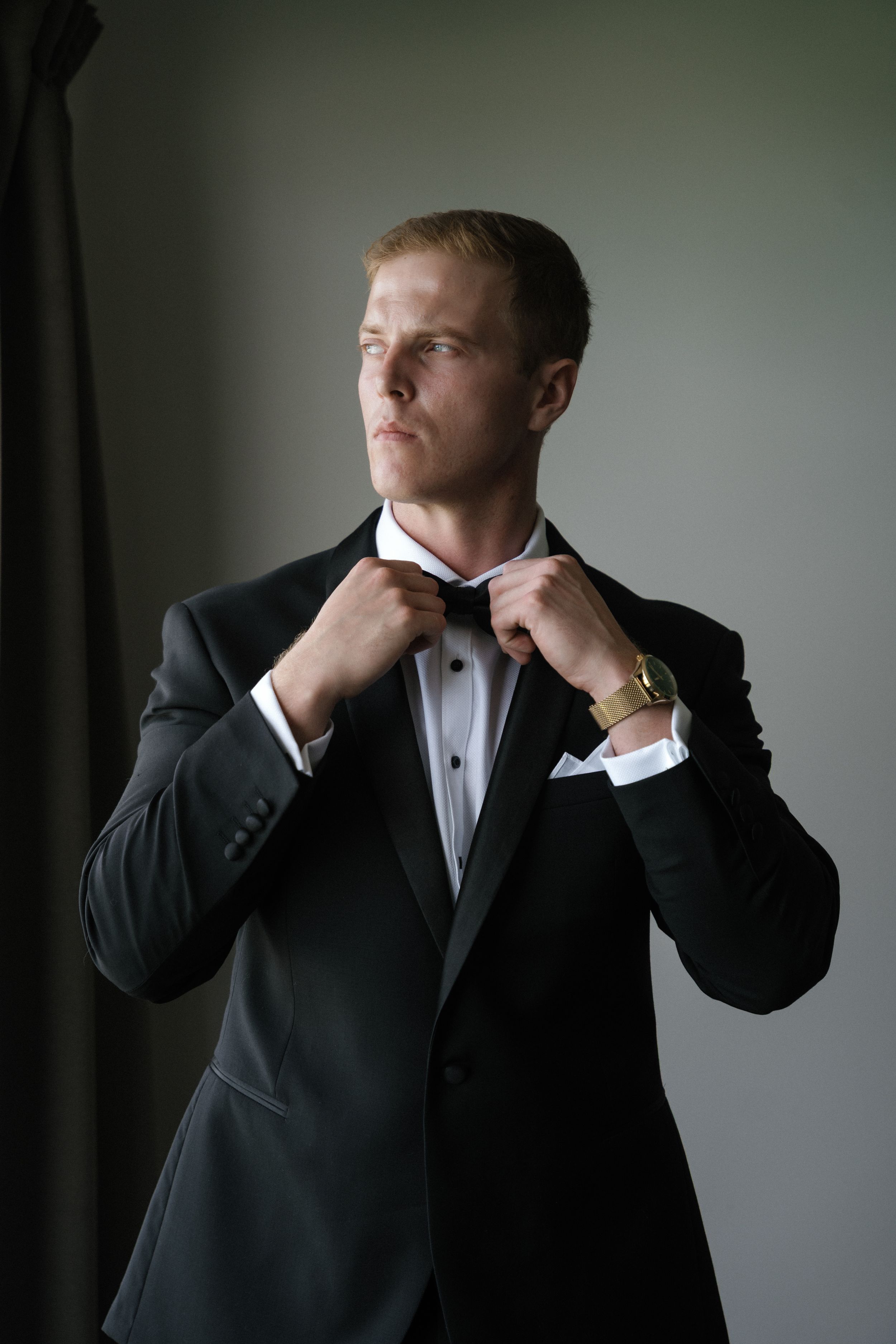 A person in a black suit and white shirt adjusts their collar in a dramatic lighting sequence.