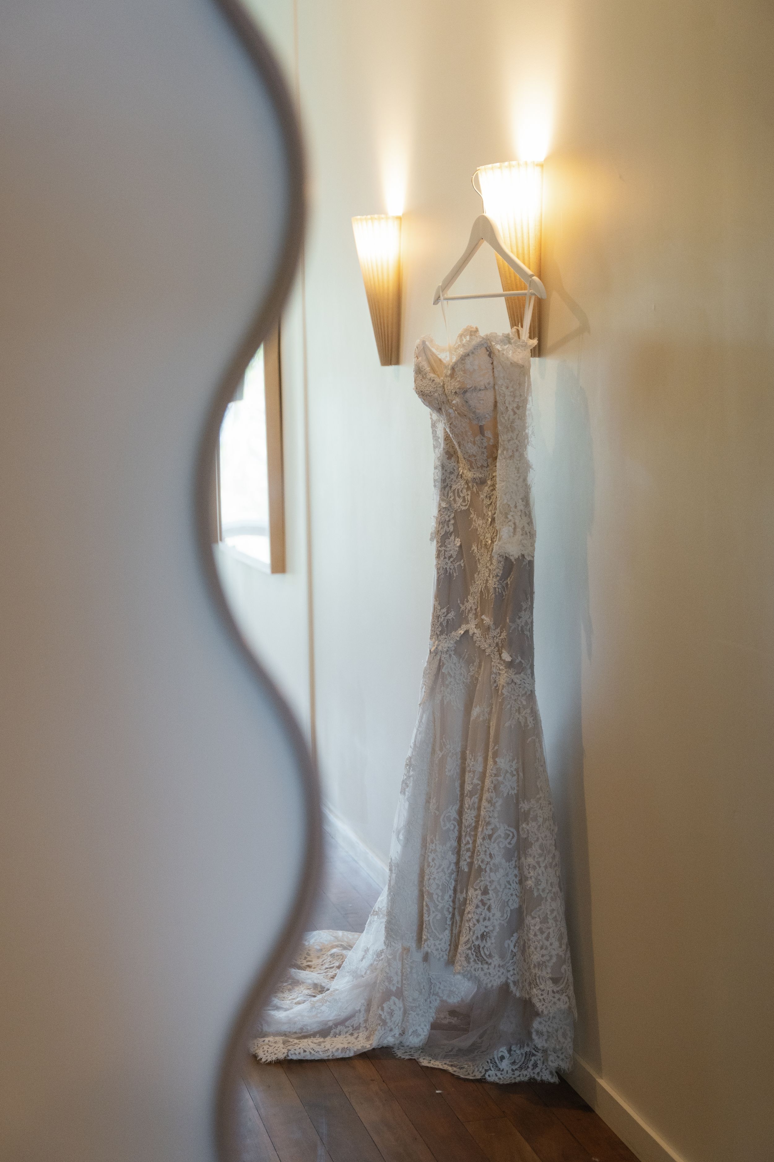 An elegant white lace wedding dress hangs on display in a corner, illuminated by warm wall sconces.