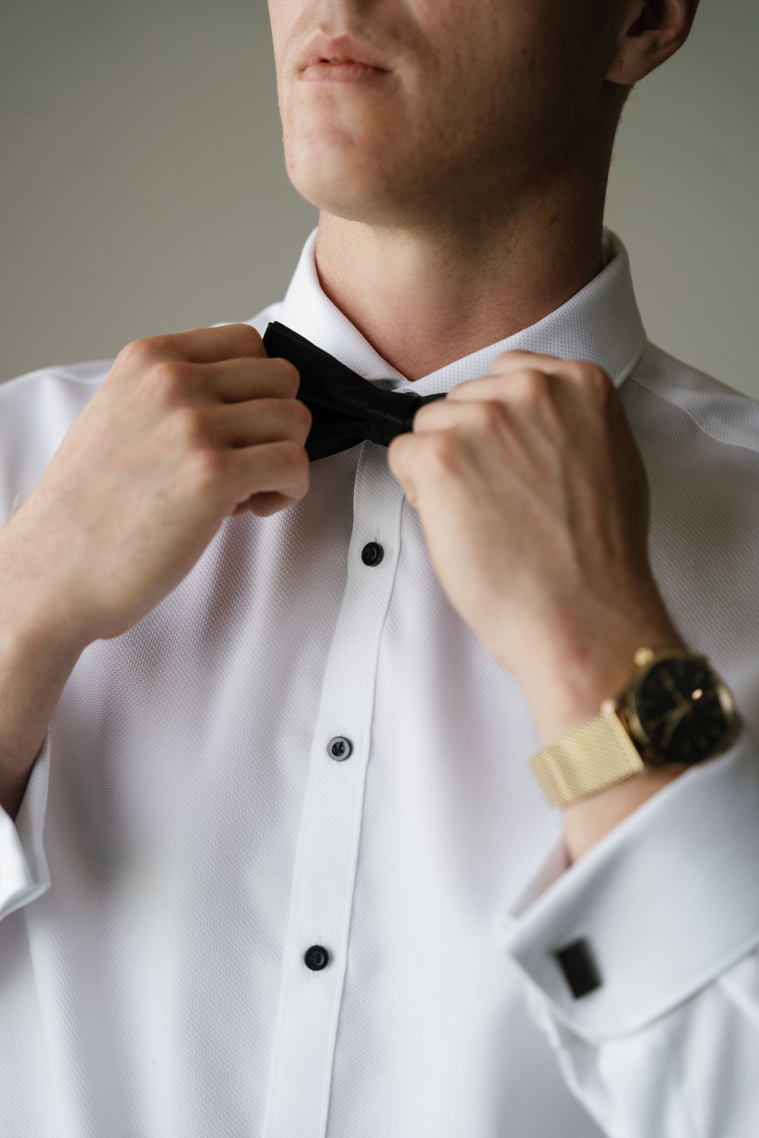 A sequence of photos showing hands adjusting a black bowtie against a crisp white formal shirt.