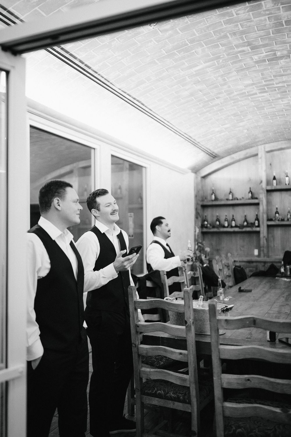 A series of black and white photos showing people in formal attire conversing in an elegant room with bottles on shelves.