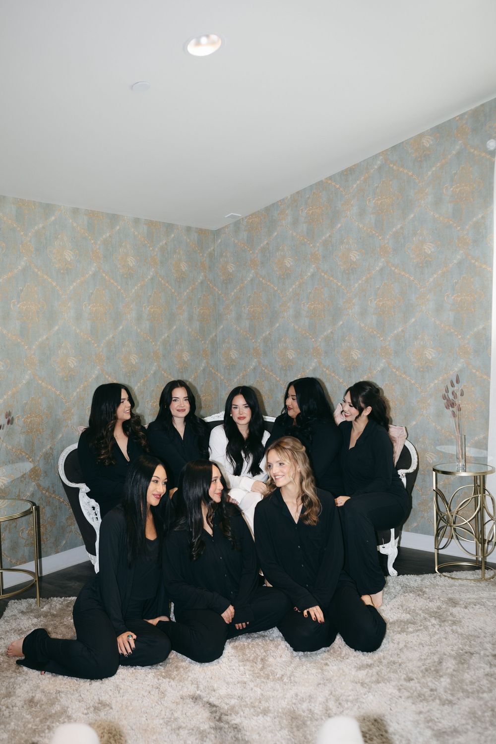Group wearing matching black outfits lounges together on plush carpet in an elegant room.