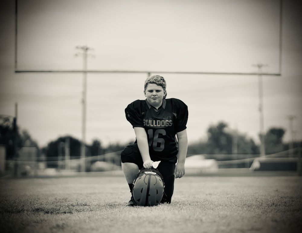 Black and white photo of a football player in a Falcons uniform kneeling on the field with a football.