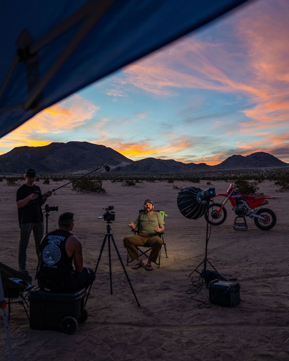 Silhouettes of photographers with telescopes and cameras capturing a vibrant desert sunset against mountain backdrop.