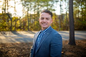 Professional outdoor portrait session in autumn forest setting with golden sunlight filtering through trees.