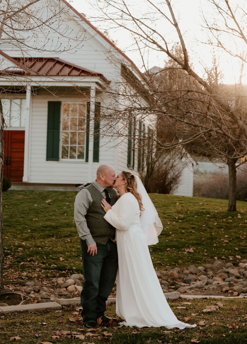 A couple shares a romantic moment during their wedding photoshoot at a rustic white farmhouse in autumn.