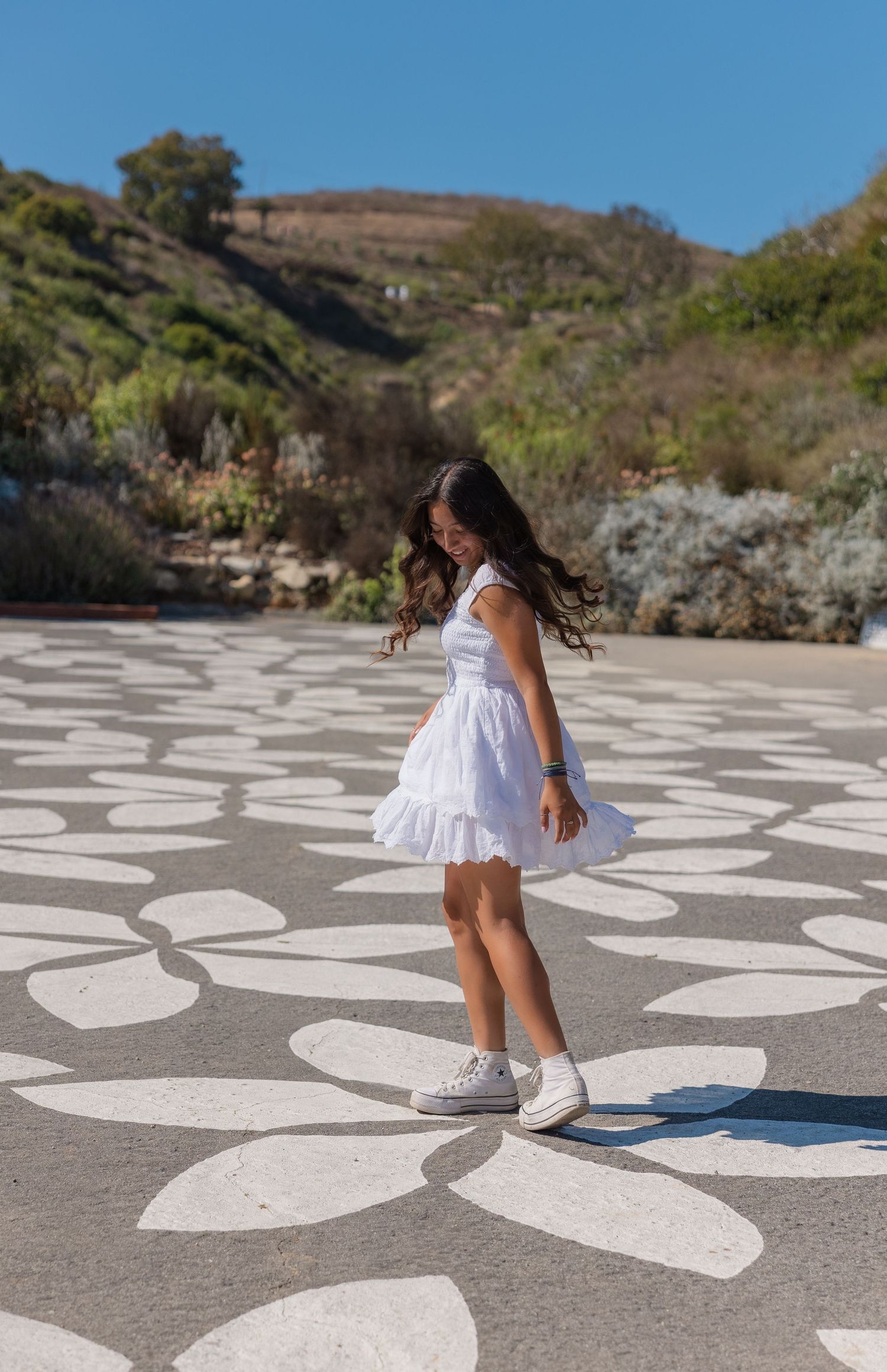 A series of images showing someone posing on a large-scale ground art installation featuring white flower patterns on concrete.