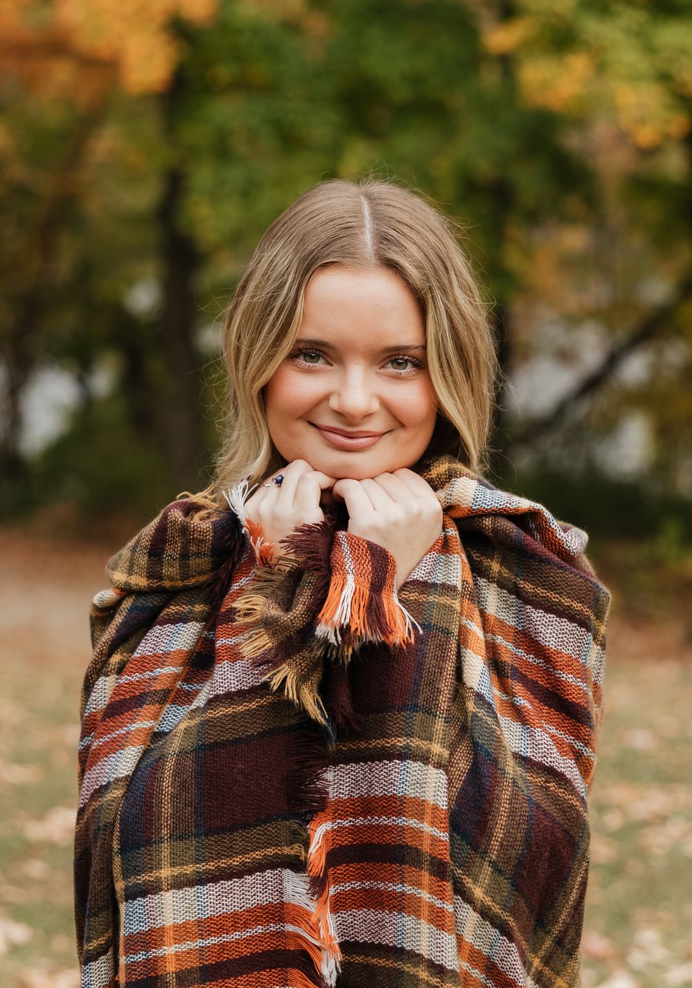 A person wrapped in a cozy plaid blanket with autumn colors enjoys a warm moment outdoors during fall.