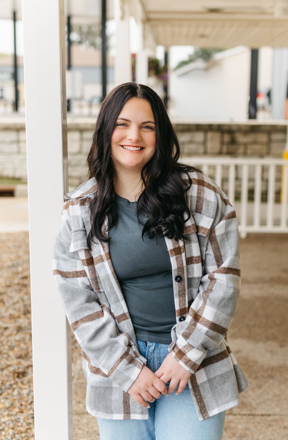 A casual autumn outfit featuring a plaid shacket, dark top and jeans in an outdoor setting.