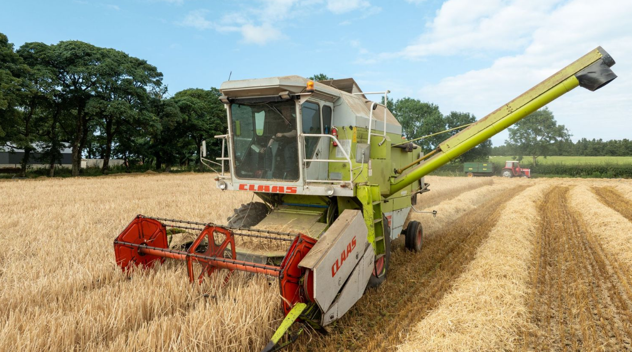 John Deere tractor with agricultural implements preparing soil in a large field under cloudy skies.