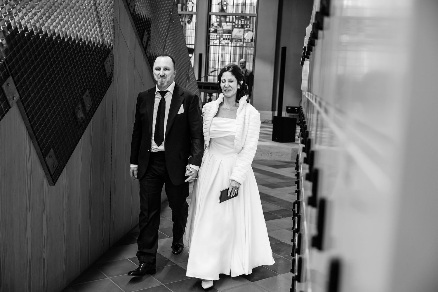 Black and white wedding photo showing bride and groom walking through an elegant corridor with decorative gates.