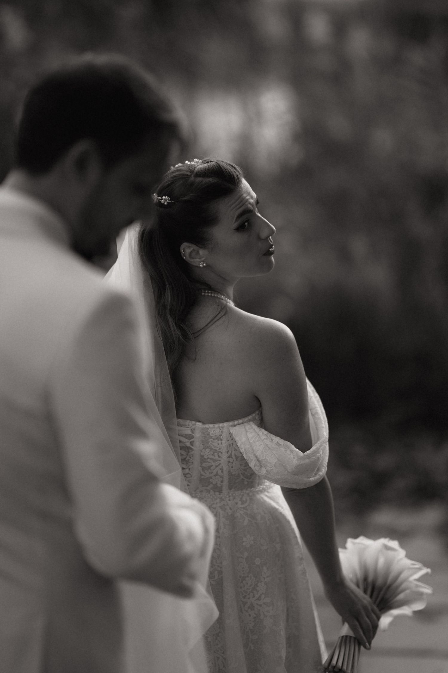 A romantic wedding couple dances in a lush garden setting as the bride's white veil flows gracefully in the breeze.