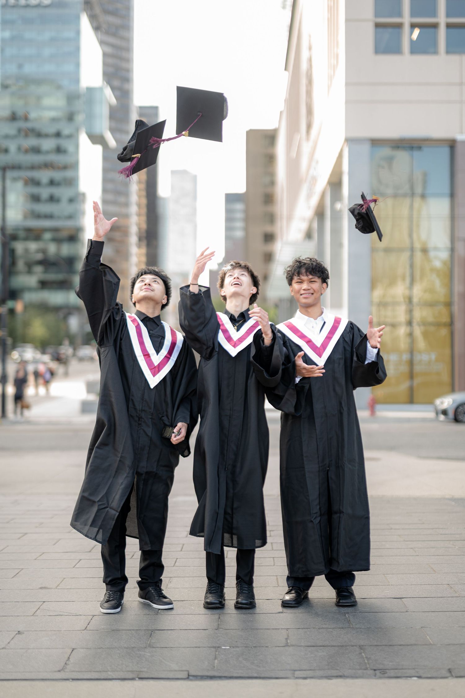 A group of graduates in black gowns and pink stoles celebrate their graduation by throwing their caps in the air.