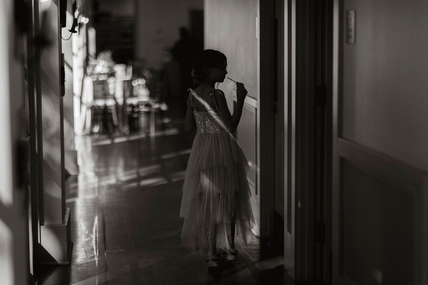 Dark moody black and white image of a corridor with silhouettes of people visible in the shadows.