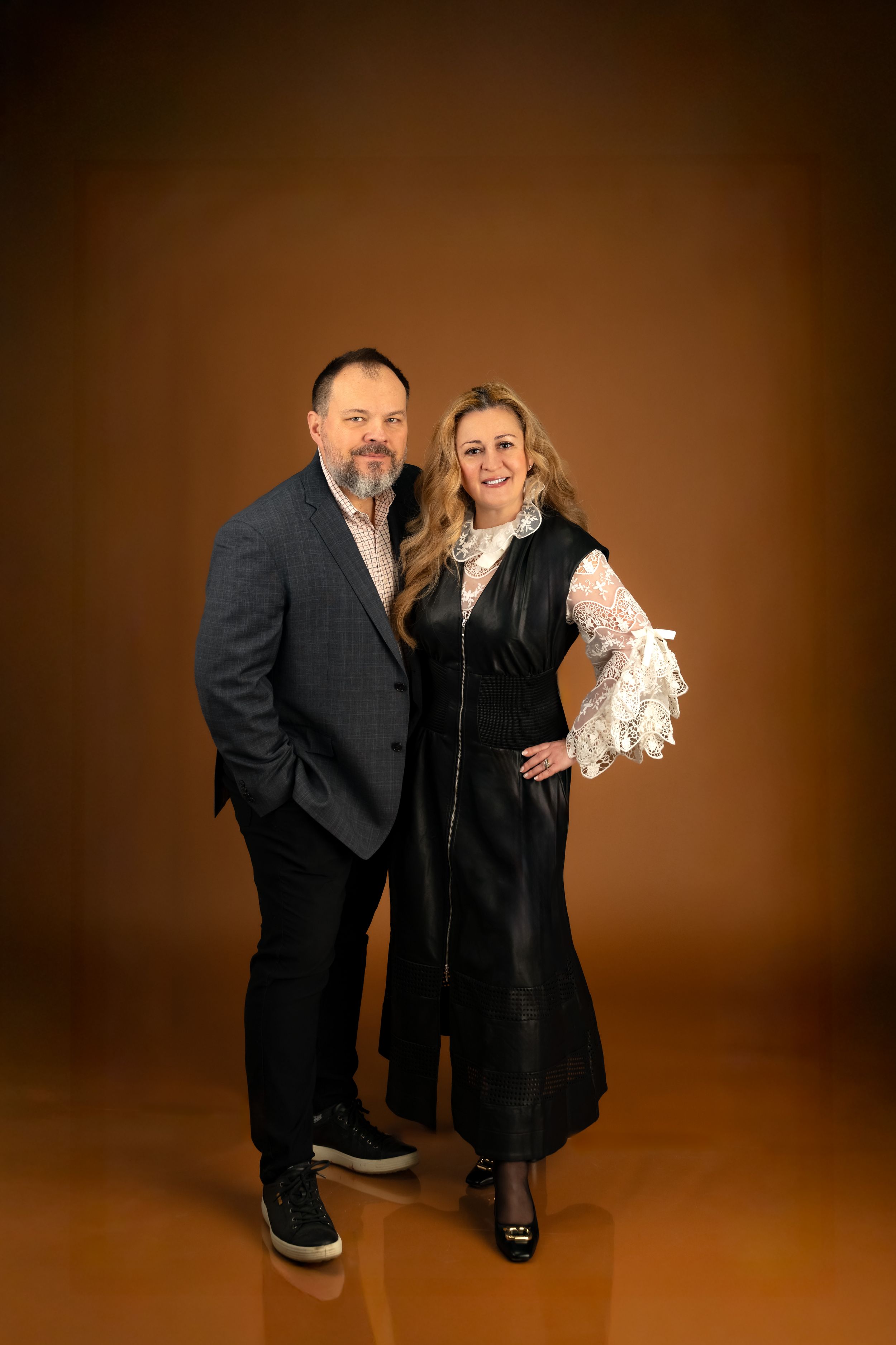 Two people in black attire pose playfully against a brown studio backdrop in a series of four connected photos.