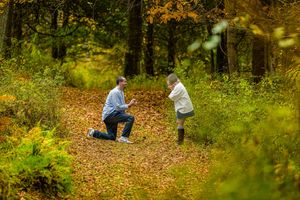 Two people sit together surrounded by colorful autumn foliage in a peaceful forest setting.
