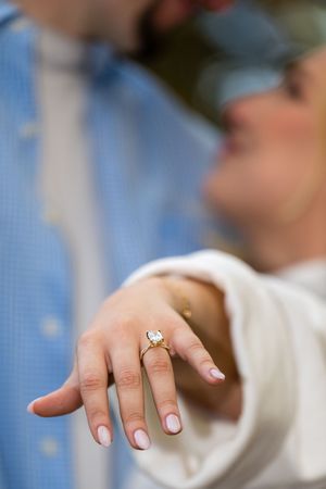 Close-up sequence showing an engagement ring being placed on a hand with a light pink manicure and white sleeve.