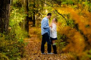 A couple walks hand in hand along a scenic autumn forest path with golden foliage overhead.