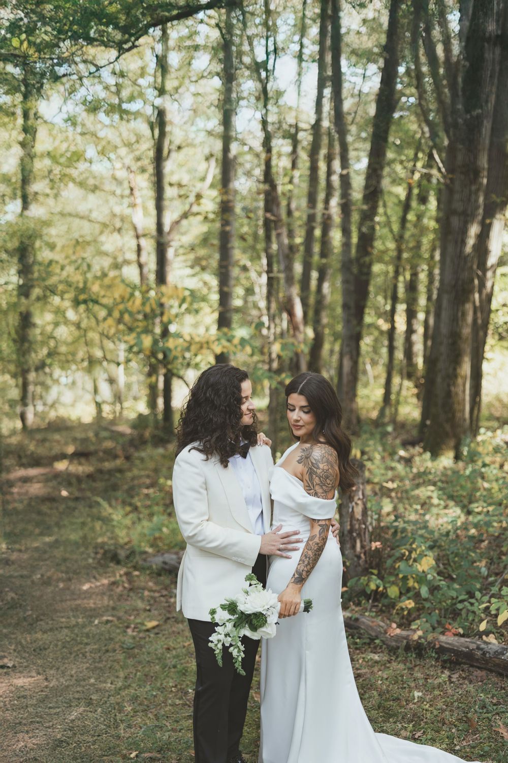 Two people in white dresses embrace during an intimate forest wedding photoshoot.