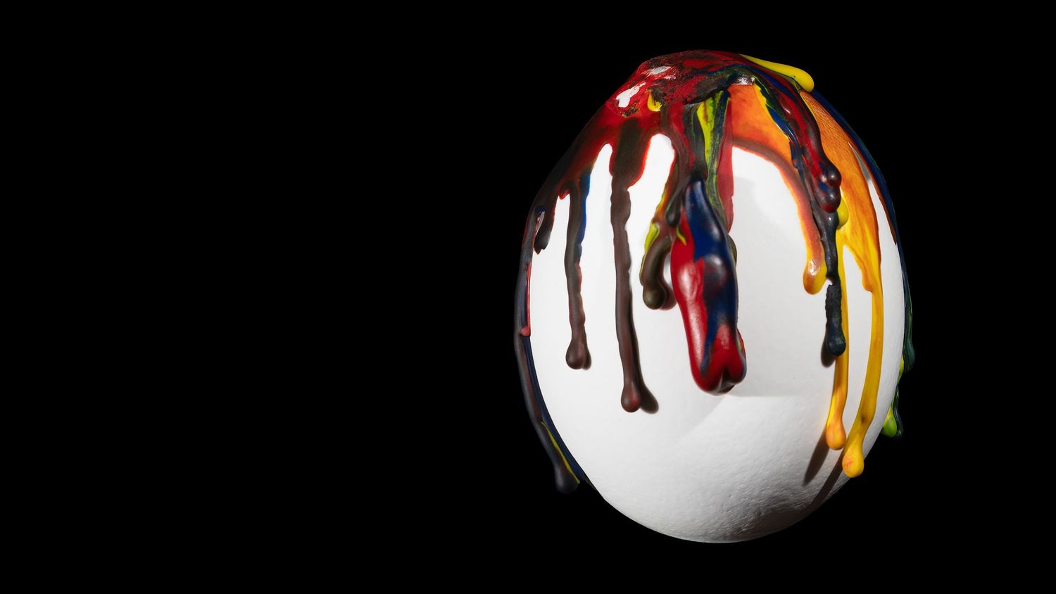 Colorful paint drips falling against a black background create a striking abstract pattern.