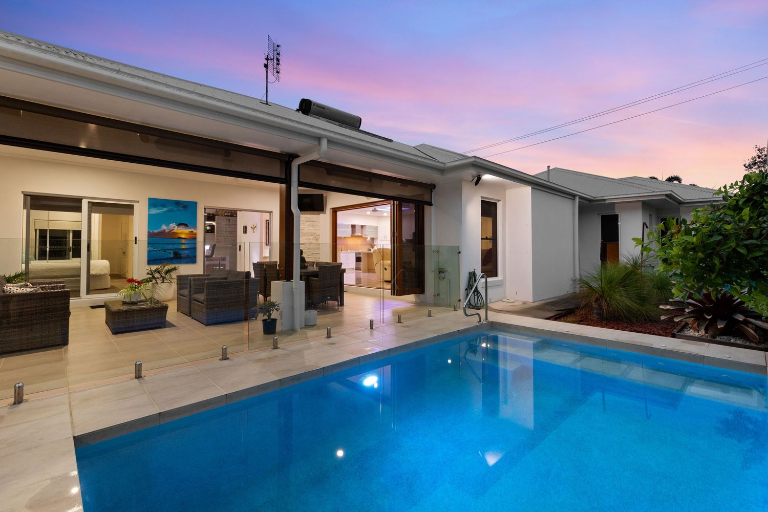 Luxurious outdoor pool with travertine paving and open-plan living area at twilight.