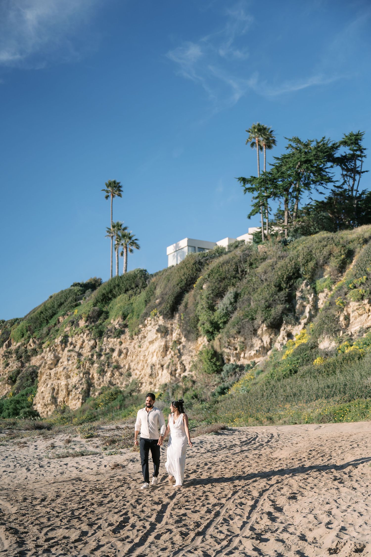 Couple walking along scenic beach with palm trees and cliffs in Orange County during sunset.