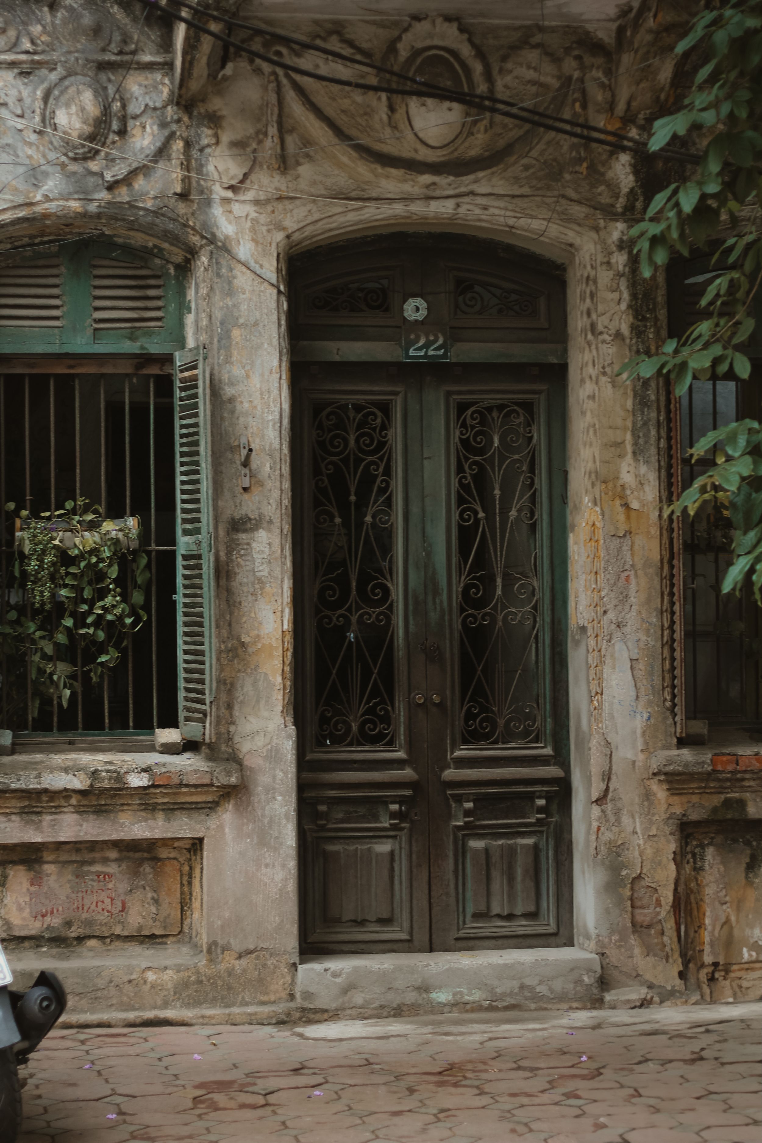 Weathered ornate double doors with wrought iron details and green shutters on old colonial style building facade.