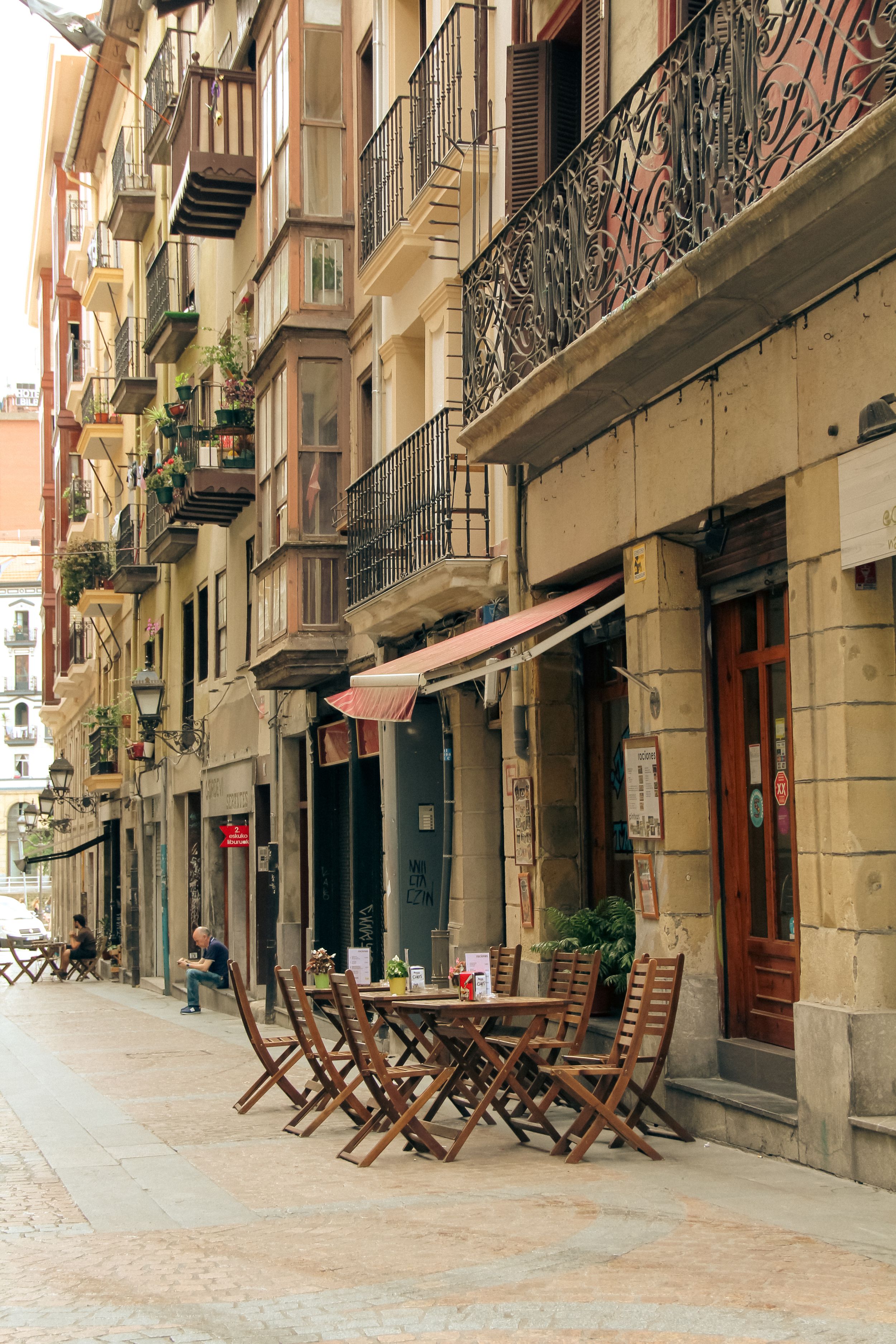 Charming European street with traditional balconies and outdoor cafe seating.