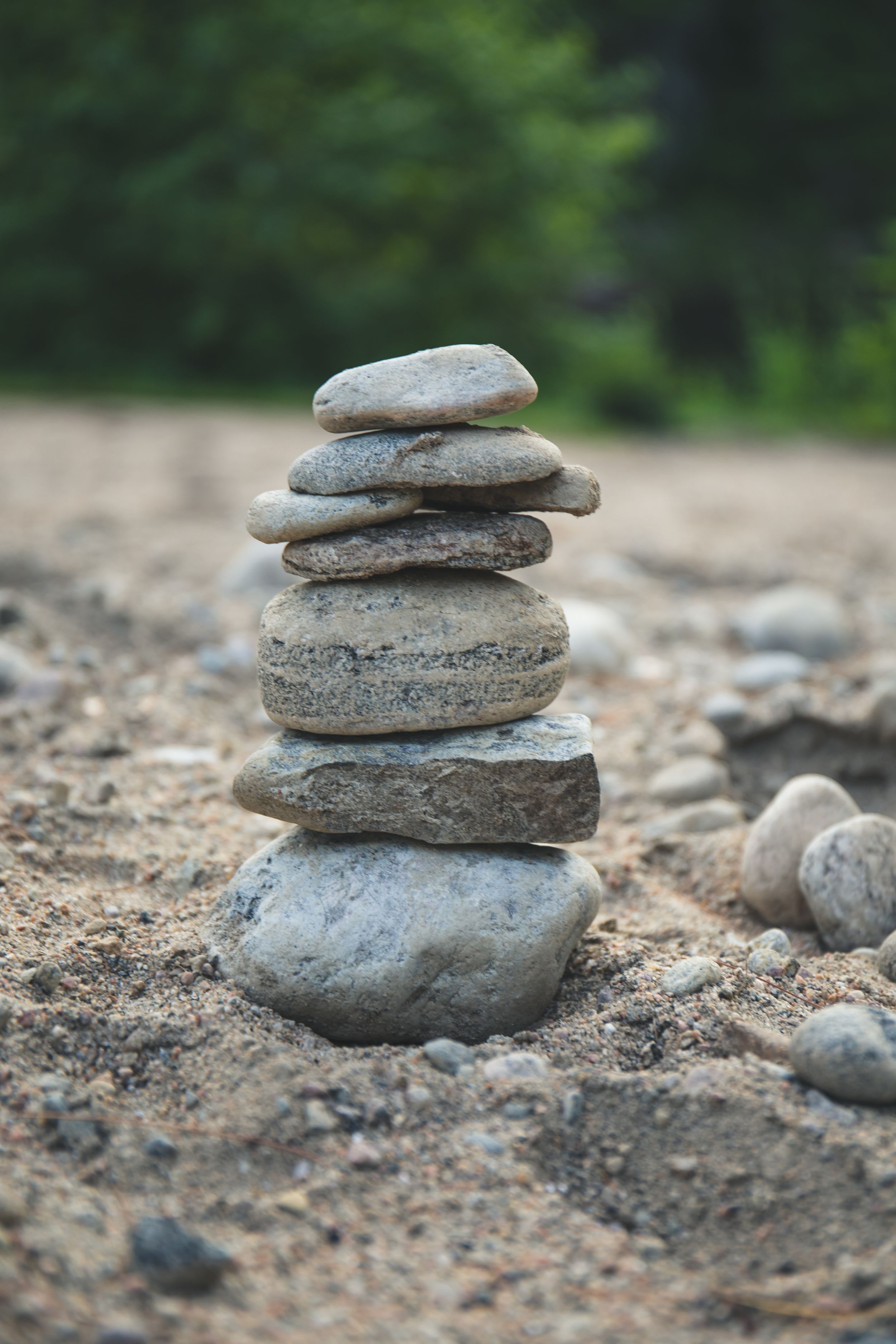 Balanced stack of natural gray stones on rocky ground with blurred green background.