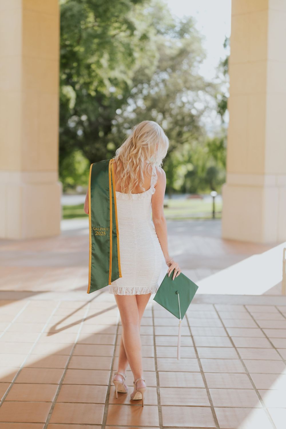A figure in a short white dress walks through an elegant covered walkway with arched columns and stone flooring.