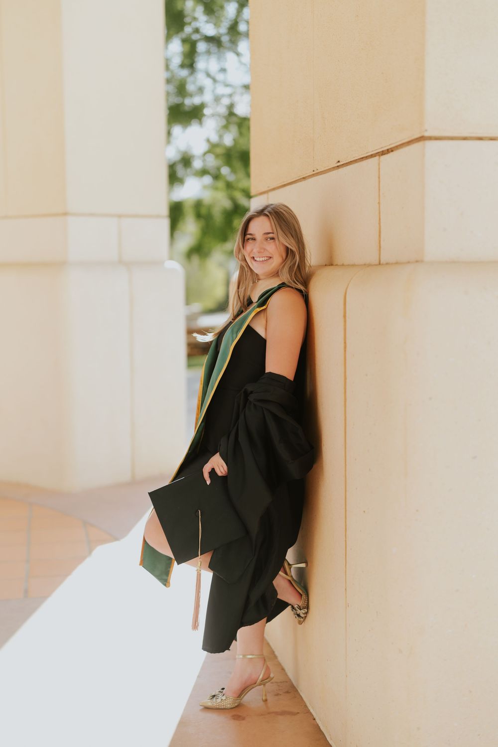 Woman in black dress poses by white pillars in romantic photoshoot series with natural lighting.