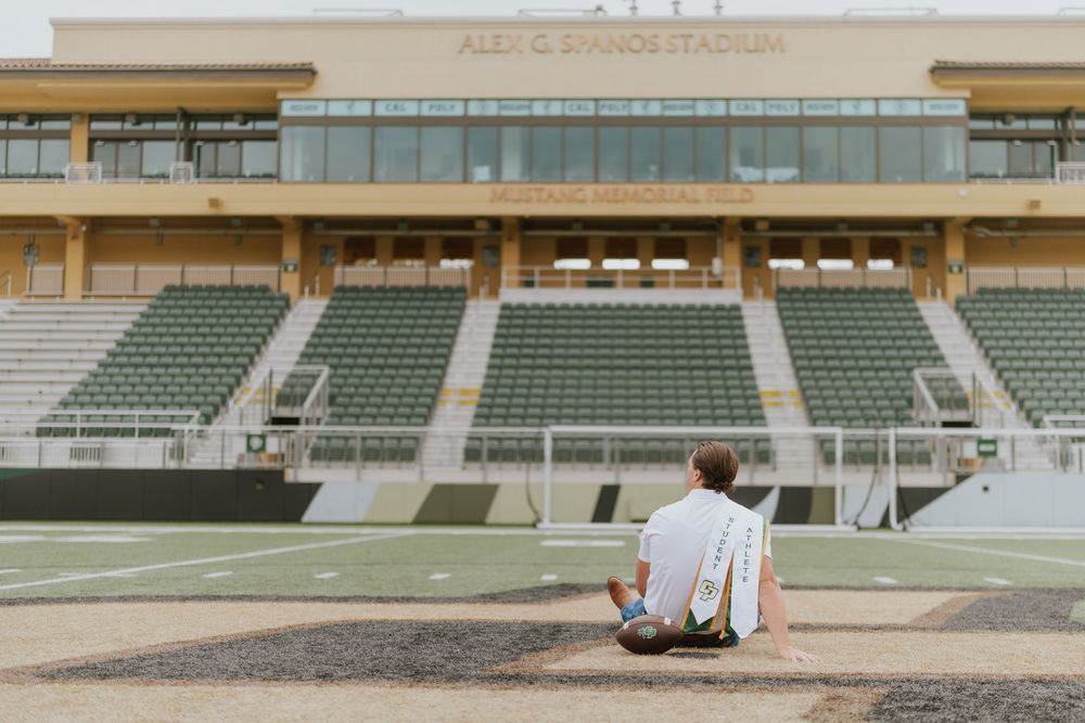 Person sits alone facing empty stadium bleachers on sunny day at athletic stadium.