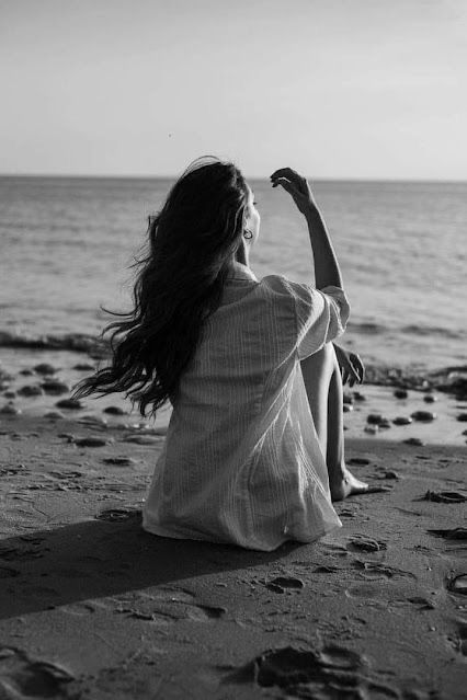 Person sitting on a beach at sunset with long flowing hair in black and white photography.