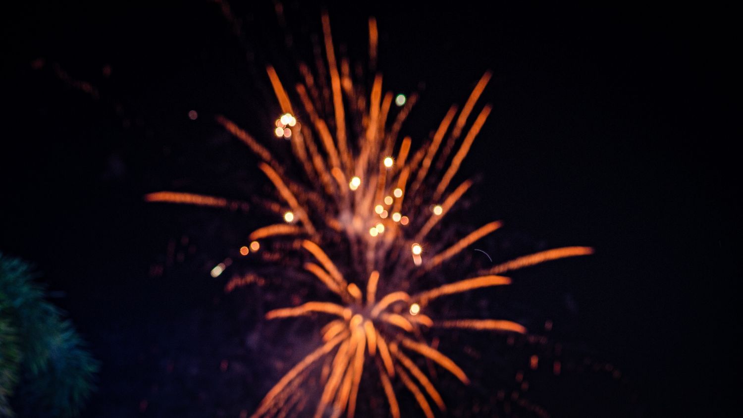 Close-up shot of bright orange fireworks bursting against a dark night sky.