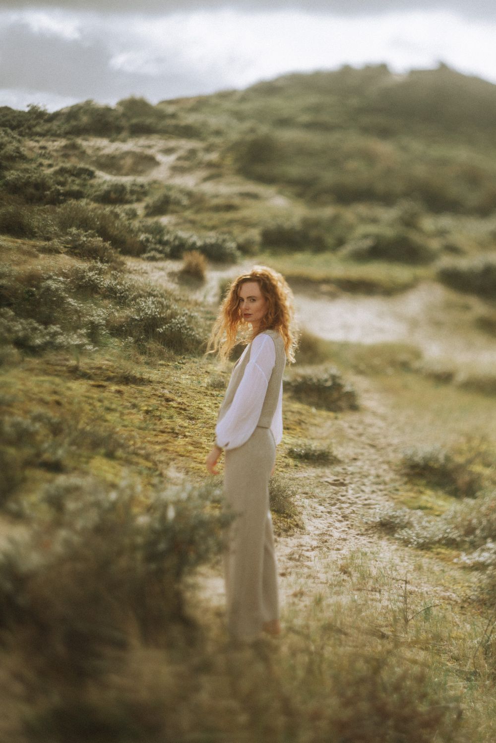 Person in white dress standing in misty coastal grasslands during golden hour.