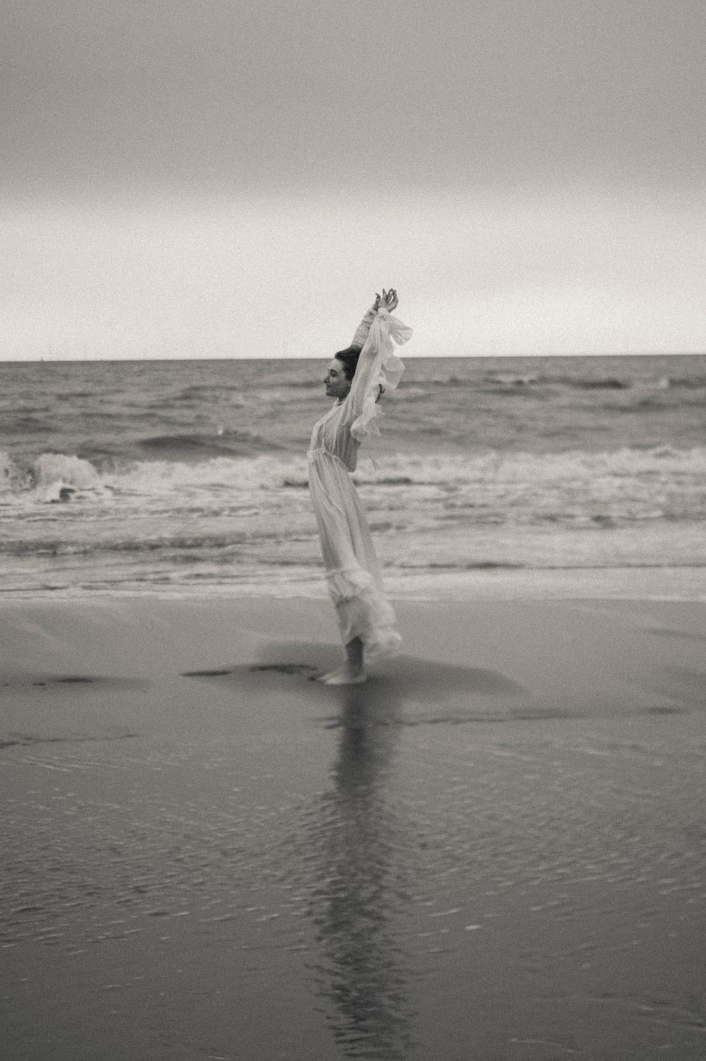 Black and white photo of person dancing in shallow ocean water.