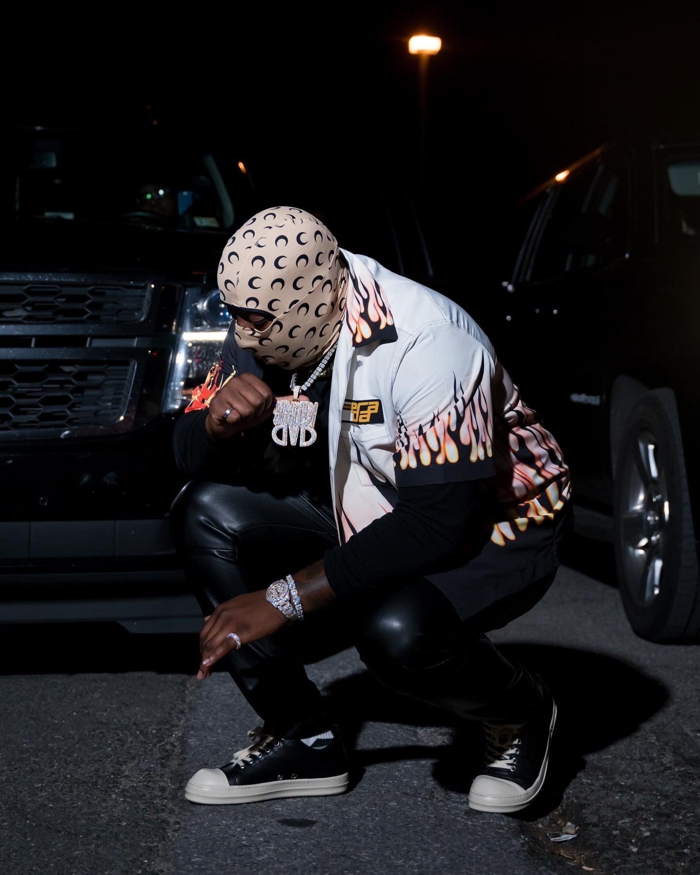 Person in white patterned jacket crouching next to car at night.
