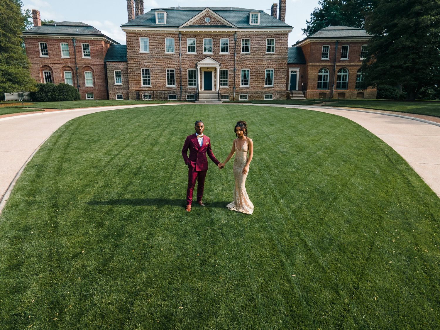 Aerial view of couple on manicured lawn in front of Georgian-style brick buildings.