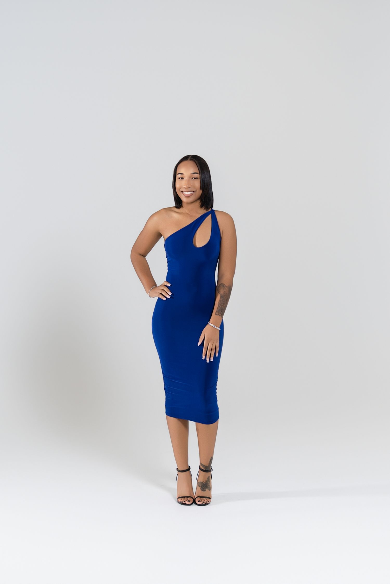 Woman in a form-fitting blue one-shoulder dress poses against white background.