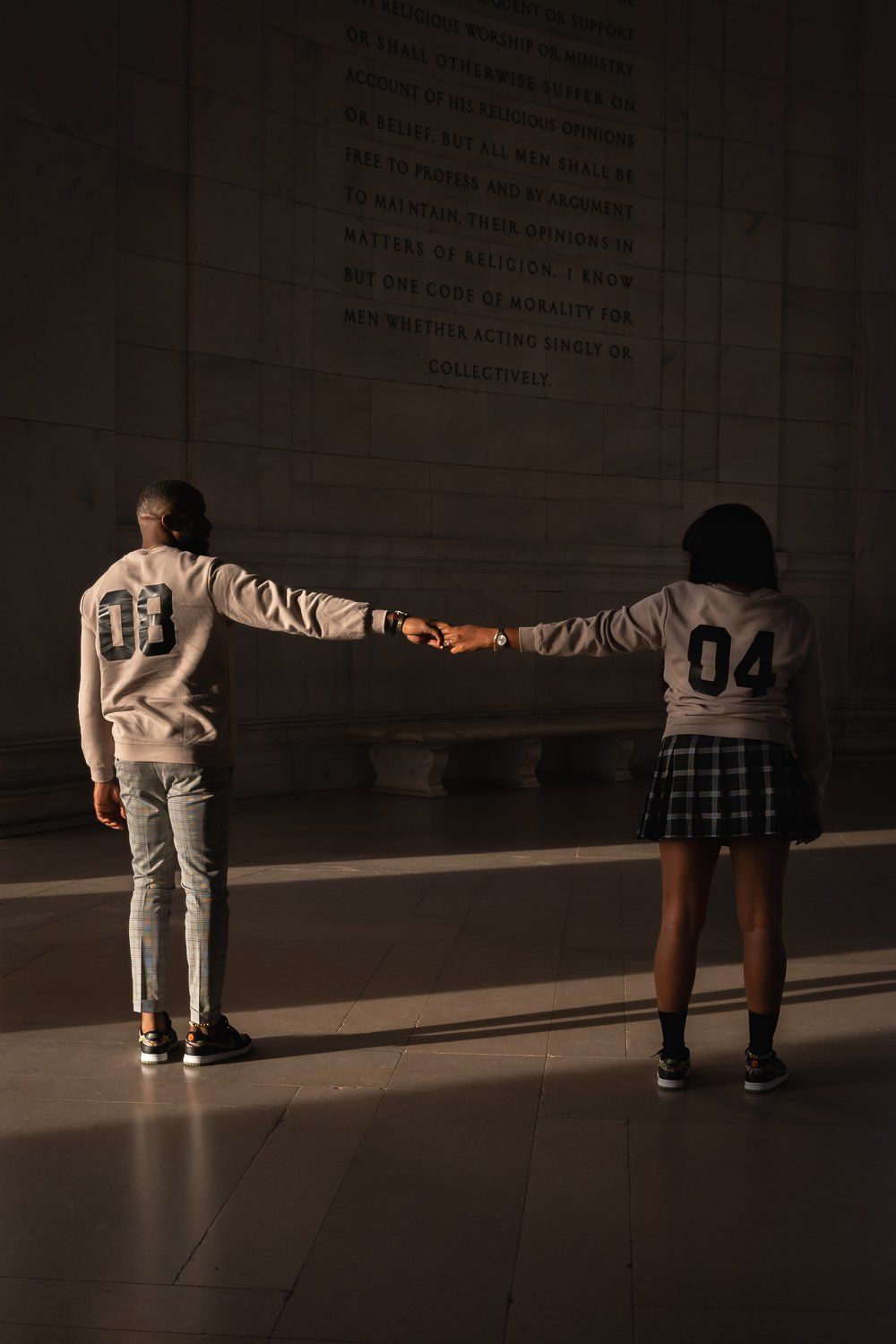 Two people in casual attire holding hands in a dimly lit indoor space.